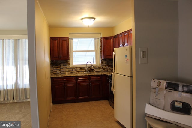 kitchen featuring backsplash, light stone counters, sink, white refrigerator, and range with electric stovetop