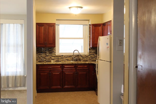 kitchen with plenty of natural light, white refrigerator, light stone countertops, and sink