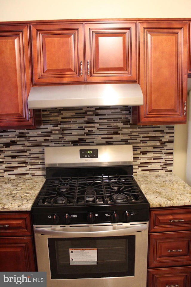 kitchen featuring backsplash, light stone counters, and stainless steel gas range oven