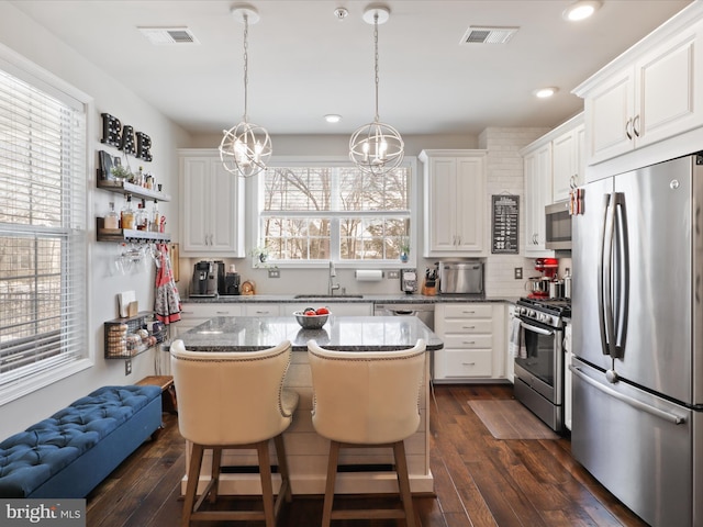 kitchen with a kitchen island, white cabinets, decorative light fixtures, and appliances with stainless steel finishes