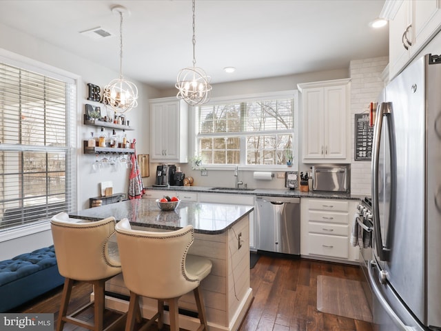 kitchen with appliances with stainless steel finishes, decorative light fixtures, white cabinets, dark hardwood / wood-style floors, and a breakfast bar area