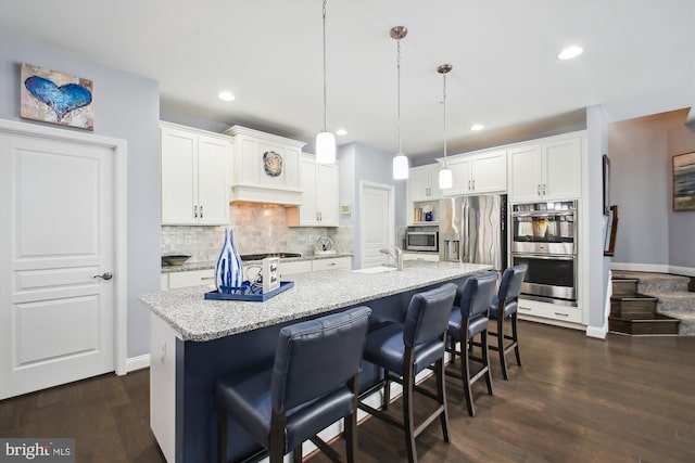 kitchen with appliances with stainless steel finishes, a kitchen island with sink, white cabinetry, and decorative light fixtures