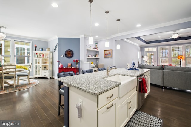 kitchen featuring ceiling fan, sink, hanging light fixtures, light stone counters, and a center island with sink