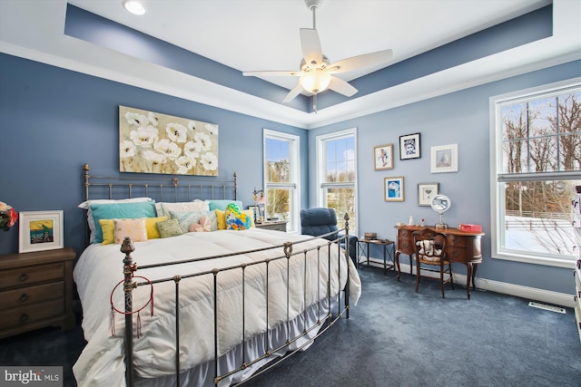 bedroom with ceiling fan, a tray ceiling, and multiple windows