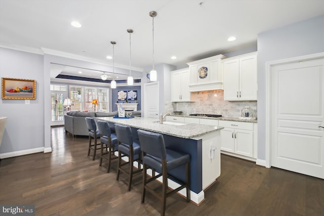 kitchen with pendant lighting, light stone countertops, white cabinetry, and an island with sink