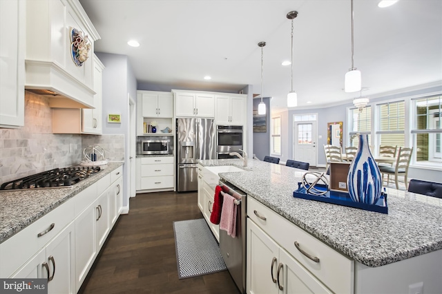 kitchen with white cabinets, appliances with stainless steel finishes, an island with sink, and pendant lighting