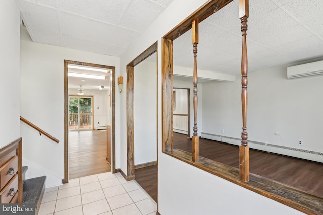 corridor featuring light tile patterned floors, an AC wall unit, a drop ceiling, and a baseboard heating unit