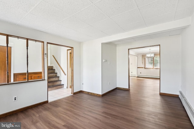 spare room featuring baseboard heating, wood-type flooring, and a notable chandelier