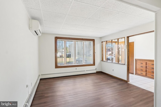 unfurnished room featuring baseboard heating, a wall mounted AC, a drop ceiling, and wood-type flooring