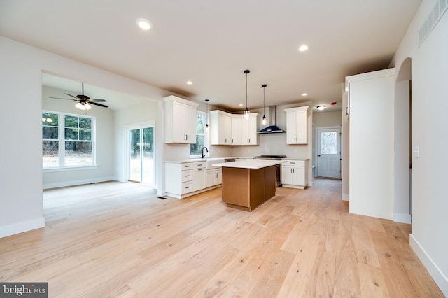 kitchen featuring wall chimney exhaust hood, sink, white cabinets, a kitchen island, and hanging light fixtures