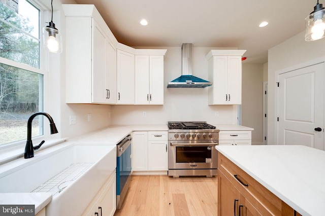 kitchen featuring sink, wall chimney exhaust hood, hanging light fixtures, stainless steel appliances, and white cabinets