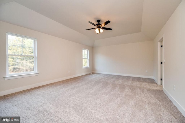 empty room featuring light carpet, a raised ceiling, ceiling fan, and a healthy amount of sunlight