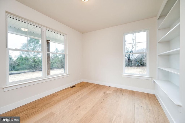 empty room featuring built in shelves, hardwood / wood-style flooring, and a wealth of natural light