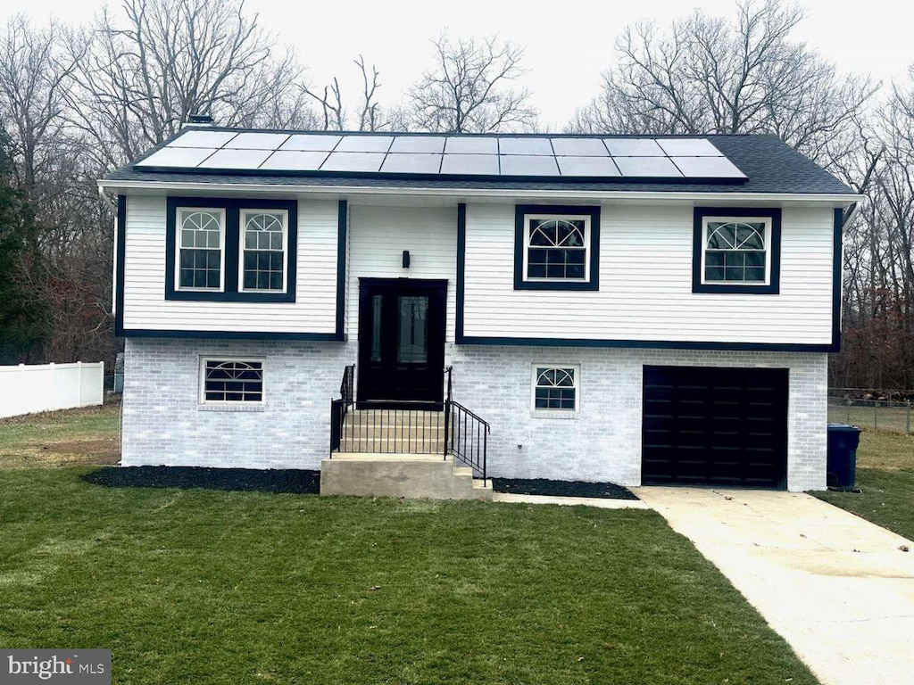 raised ranch with solar panels, a garage, and a front lawn