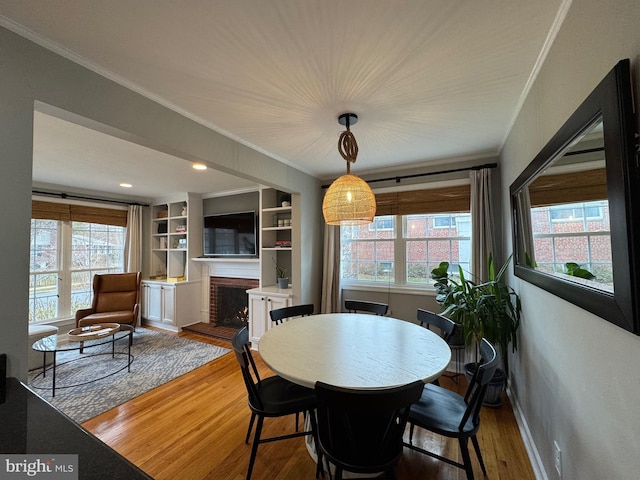 dining space with hardwood / wood-style floors, built in shelves, ornamental molding, and a fireplace