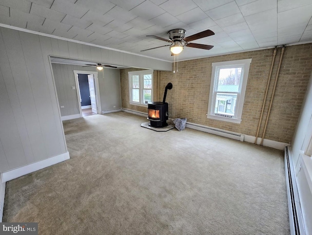 interior space with a wood stove, crown molding, brick wall, and a baseboard heating unit