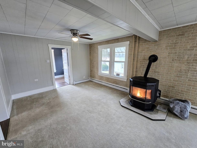 unfurnished living room with carpet flooring, a wood stove, ceiling fan, and brick wall