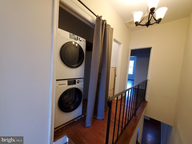 washroom with dark hardwood / wood-style flooring, stacked washer and dryer, and a notable chandelier