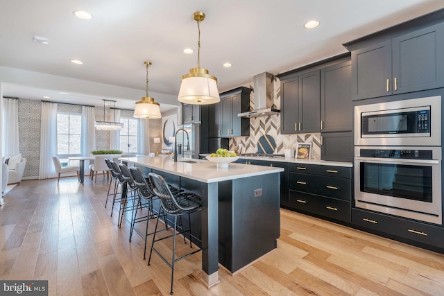 kitchen featuring appliances with stainless steel finishes, a kitchen breakfast bar, wall chimney range hood, pendant lighting, and a center island with sink