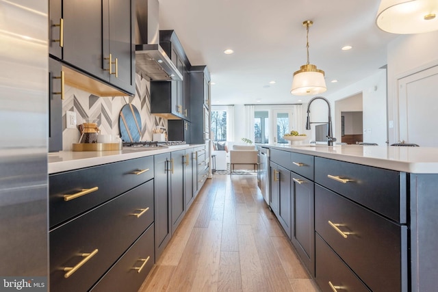 kitchen with wall chimney exhaust hood, decorative backsplash, light wood-type flooring, decorative light fixtures, and stainless steel appliances