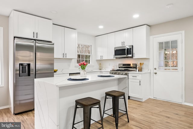 kitchen with a center island, stainless steel appliances, a breakfast bar area, white cabinets, and light wood-type flooring