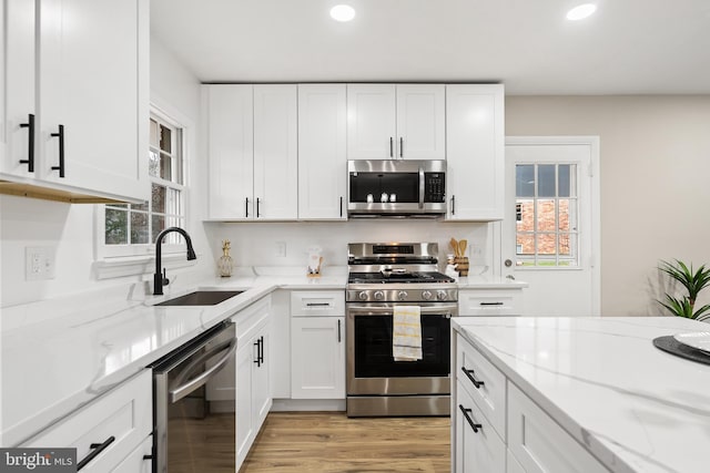 kitchen featuring light stone countertops, stainless steel appliances, sink, white cabinets, and plenty of natural light