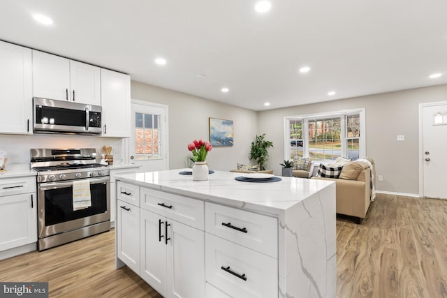 kitchen featuring light stone countertops, a center island, stainless steel appliances, light hardwood / wood-style flooring, and white cabinets