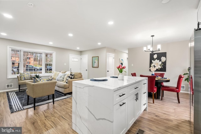 kitchen featuring light stone counters, white cabinets, light hardwood / wood-style floors, a kitchen island, and hanging light fixtures