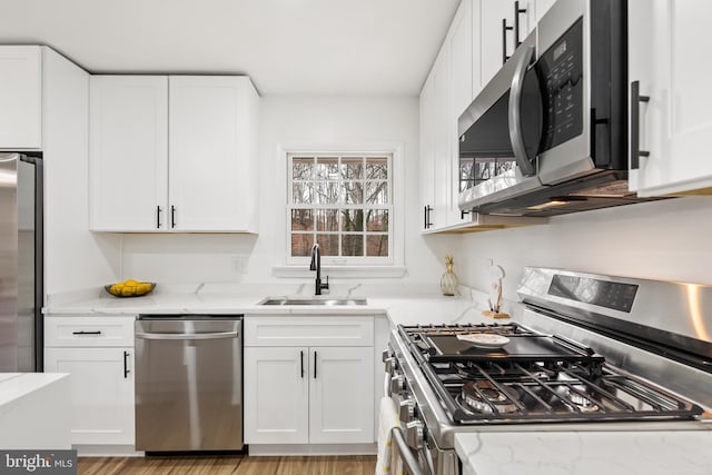 kitchen with light stone countertops, appliances with stainless steel finishes, white cabinetry, and sink