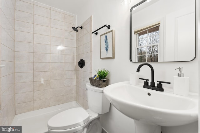 bathroom featuring tiled shower, sink, and toilet