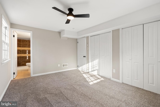 unfurnished bedroom with multiple closets, ensuite bathroom, ceiling fan, and light colored carpet