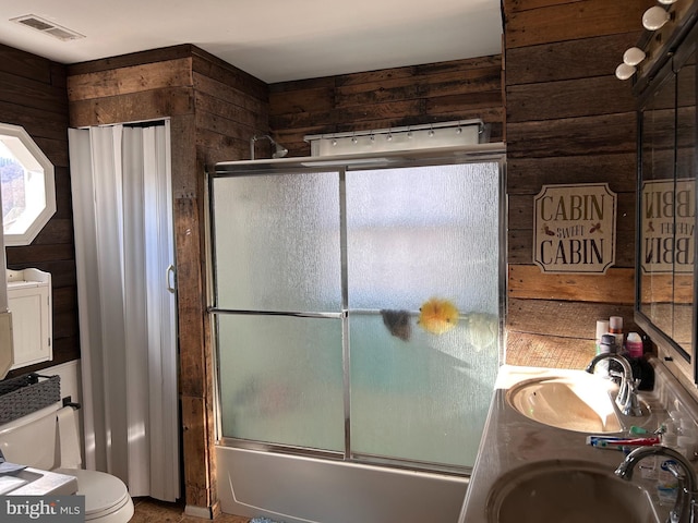 full bathroom featuring wooden walls, vanity, combined bath / shower with glass door, and toilet