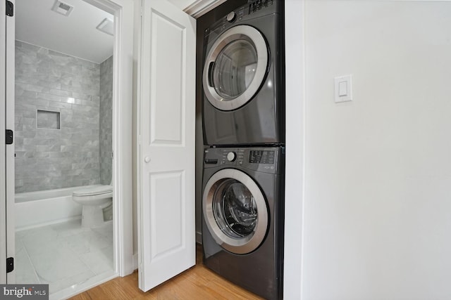 clothes washing area with light wood-type flooring and stacked washing maching and dryer