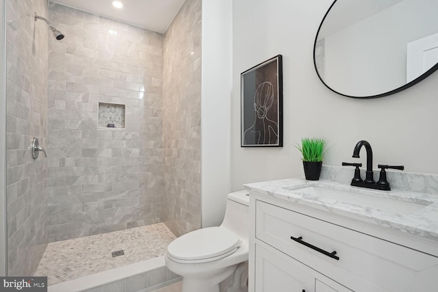 bathroom with a tile shower, vanity, and toilet