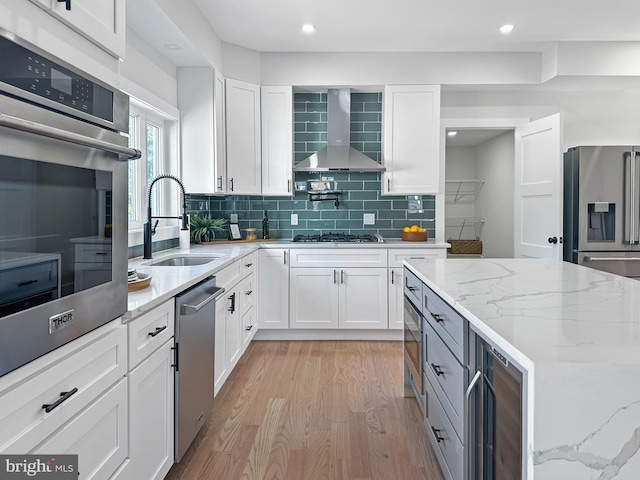 kitchen featuring white cabinets, wall chimney exhaust hood, sink, and stainless steel appliances