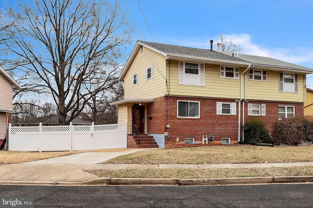 colonial home with concrete driveway, brick siding, fence, and a front lawn