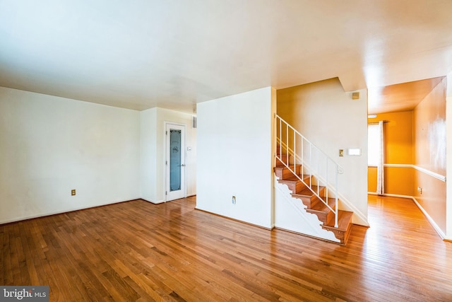 unfurnished living room featuring wood-type flooring, stairway, and baseboards