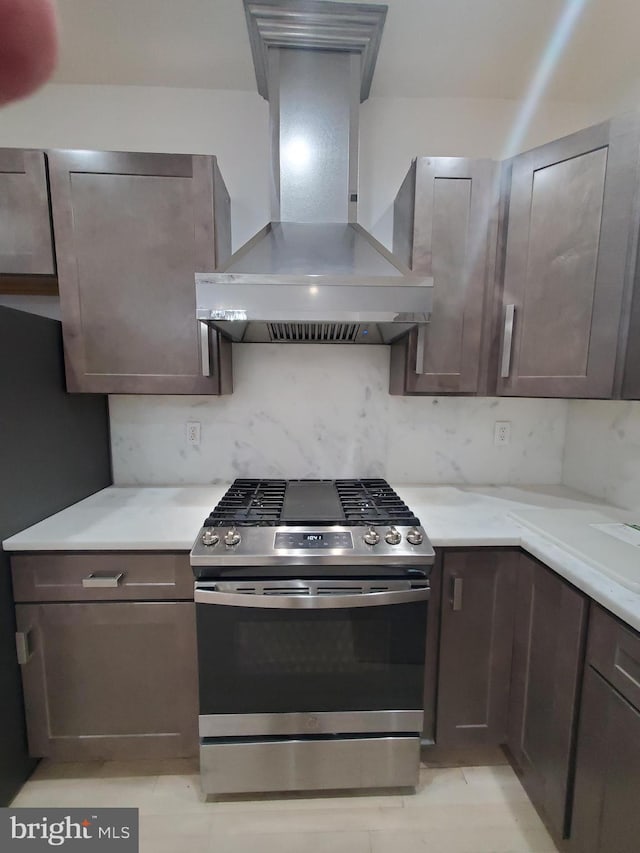 kitchen featuring decorative backsplash, dark brown cabinetry, stainless steel gas range, and wall chimney exhaust hood