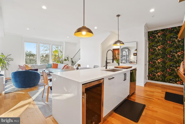 kitchen with light wood-type flooring, a kitchen island with sink, beverage cooler, sink, and decorative light fixtures