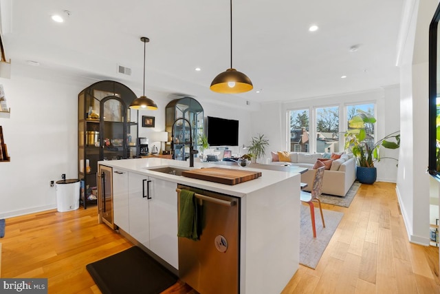 kitchen featuring sink, decorative light fixtures, a center island with sink, dishwasher, and white cabinets