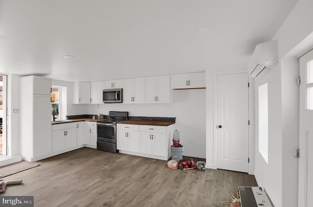 kitchen featuring light hardwood / wood-style flooring, stainless steel appliances, white cabinetry, and a wall unit AC