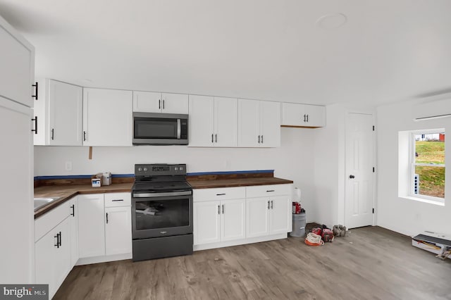 kitchen with white cabinets, light wood-type flooring, electric range, and butcher block countertops