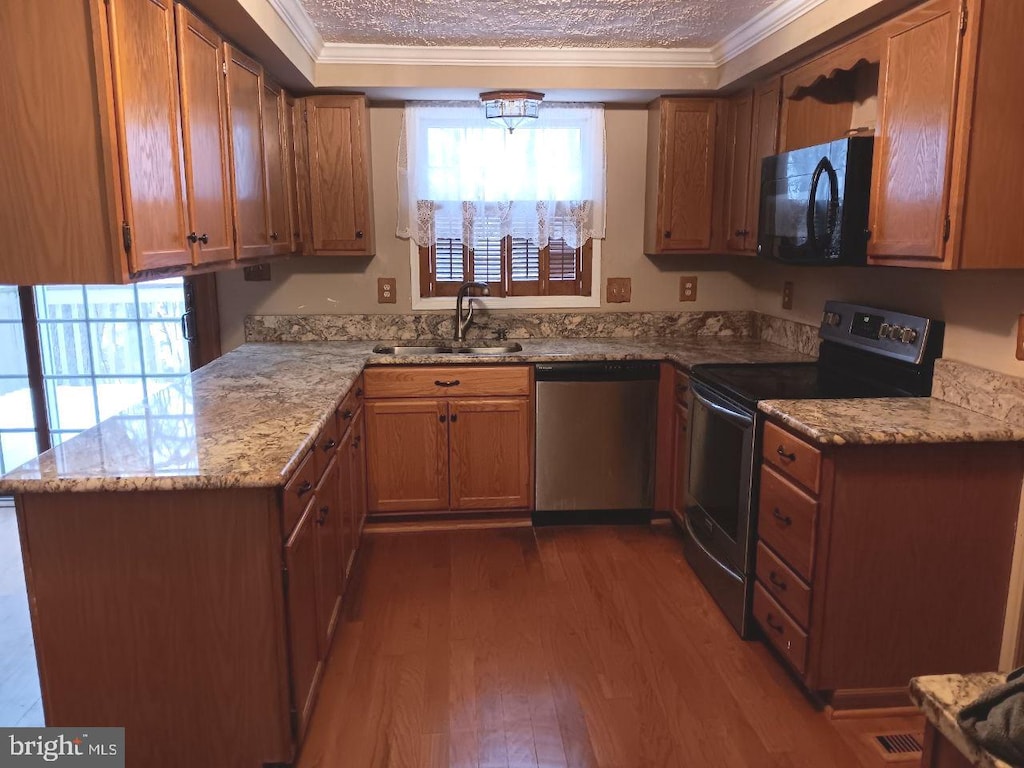 kitchen featuring sink, light stone counters, wood-type flooring, black appliances, and ornamental molding