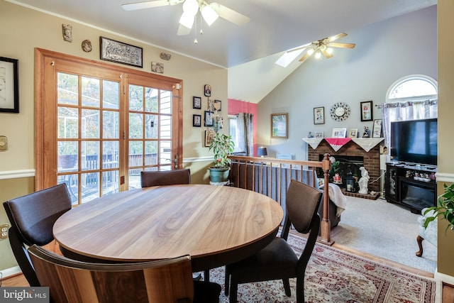 dining area featuring ceiling fan, vaulted ceiling with skylight, and a fireplace