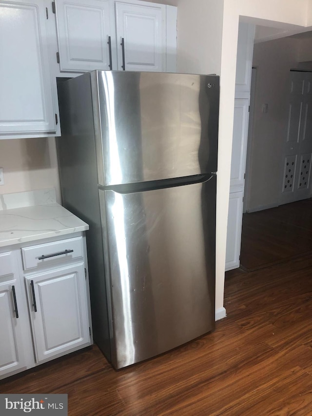 kitchen with white cabinets, dark hardwood / wood-style flooring, light stone countertops, and stainless steel refrigerator