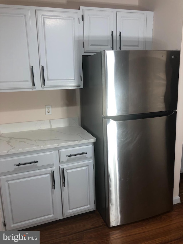 kitchen featuring white cabinets, dark hardwood / wood-style floors, stainless steel refrigerator, and light stone countertops