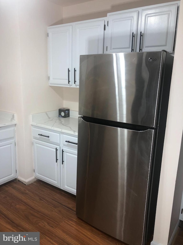 kitchen with stainless steel fridge, light stone counters, and white cabinetry