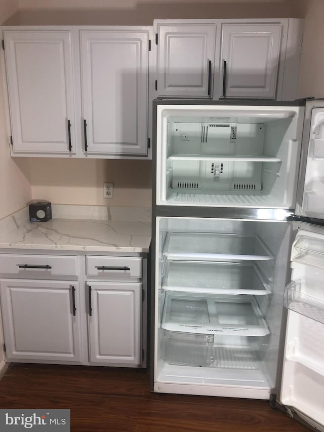 kitchen featuring light stone countertops, refrigerator, and white cabinetry