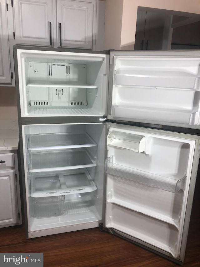 interior details featuring white cabinets, dark wood-type flooring, and fridge