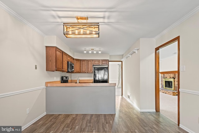 kitchen featuring kitchen peninsula, black refrigerator, hardwood / wood-style floors, a fireplace, and ornamental molding